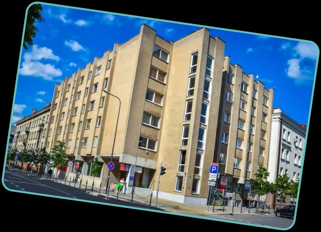 A beige multi-story apartment building with large windows stands against a bright blue sky, framed by a tilted turquoise border.