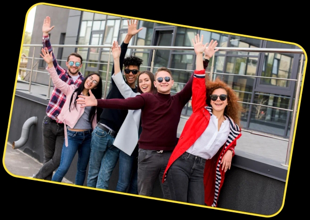 A group of six young friends in stylish casual outfits joyfully pose with raised hands and wide smiles on a modern rooftop, framed by a yellow border.